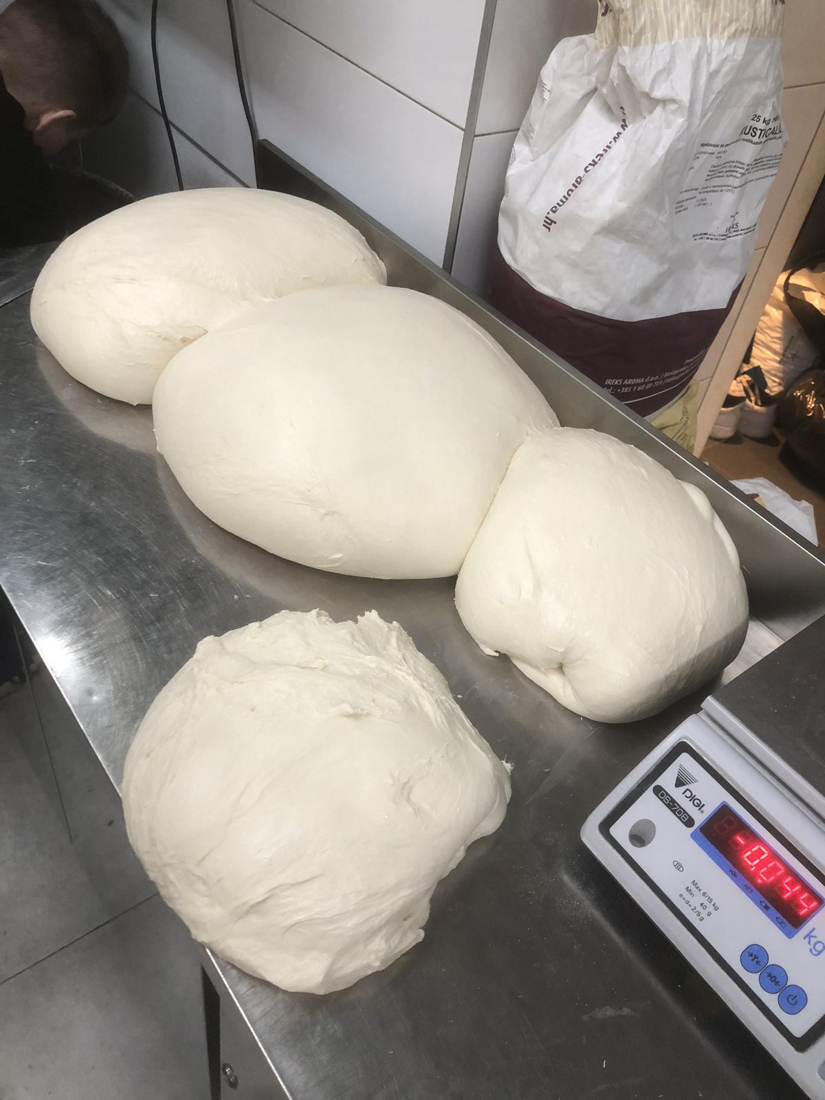 Proofed dough balls resting on a scale in a pizzeria kitchen