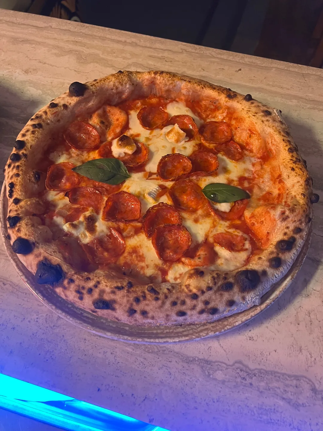 Wood-fired Neapolitan pepperoni pizza with fresh basil on a marble counter